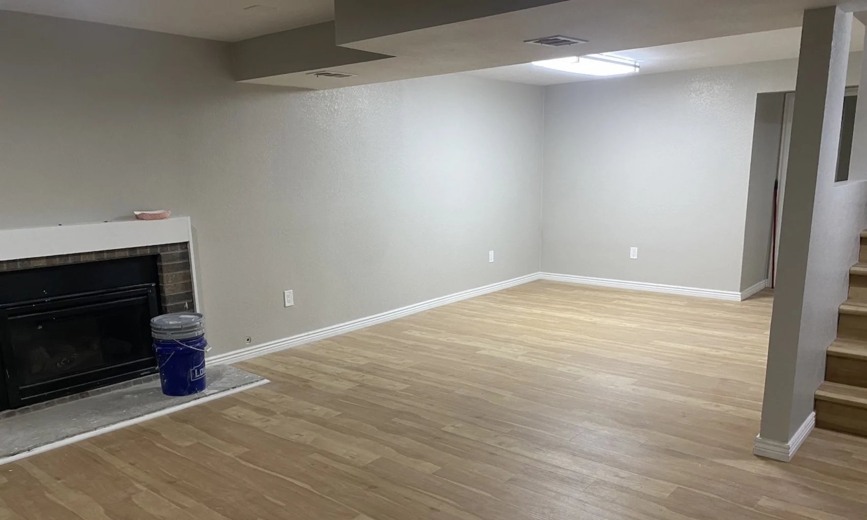 A finished basement, wood laminate floor, lighting.