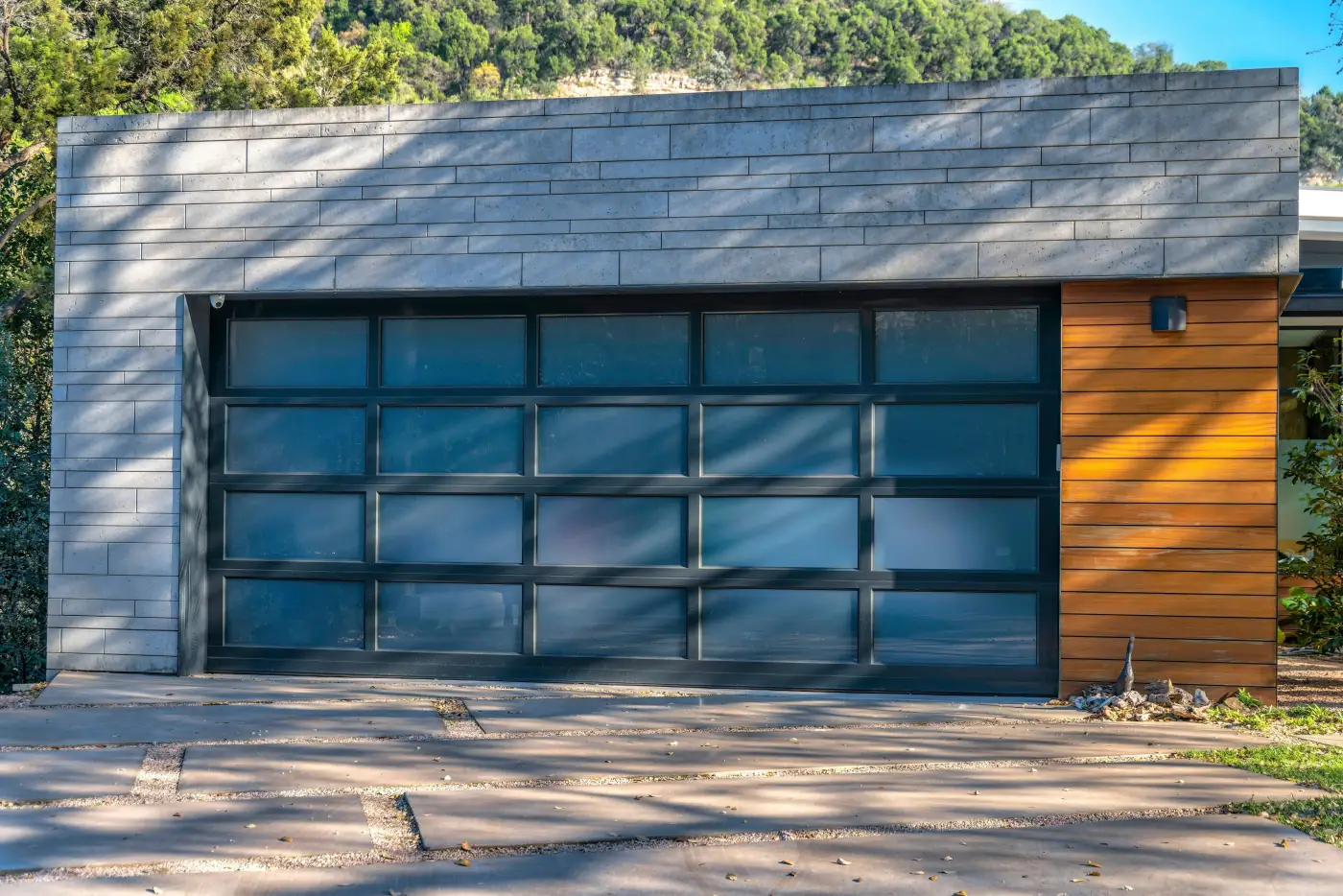 A modern garage from the outside. The exterior is built from various colored bricks, and the door has a unique design with rectangular patterns. Depicts modern garage ideas.